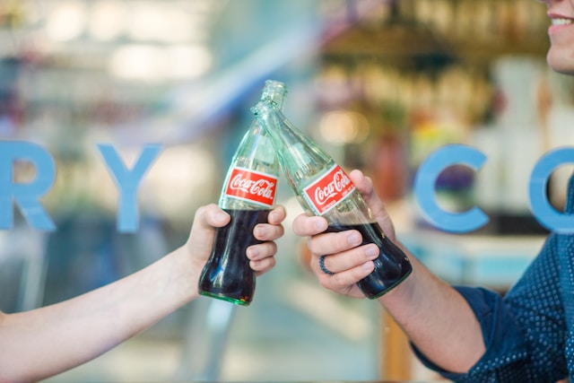 Two people clinking Coke bottles